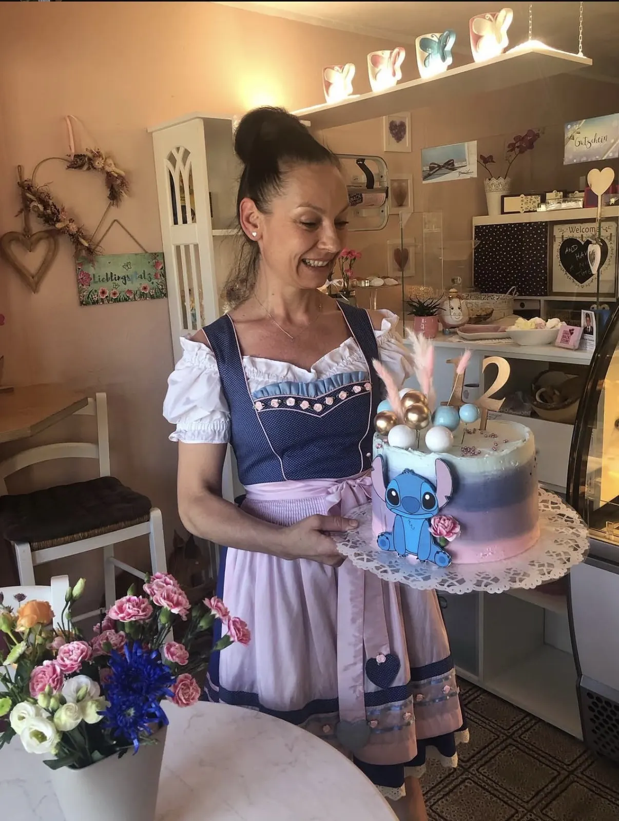 Silvia im Dirndl mit einer Stitch-Motivtorte in ihrem Geschäft