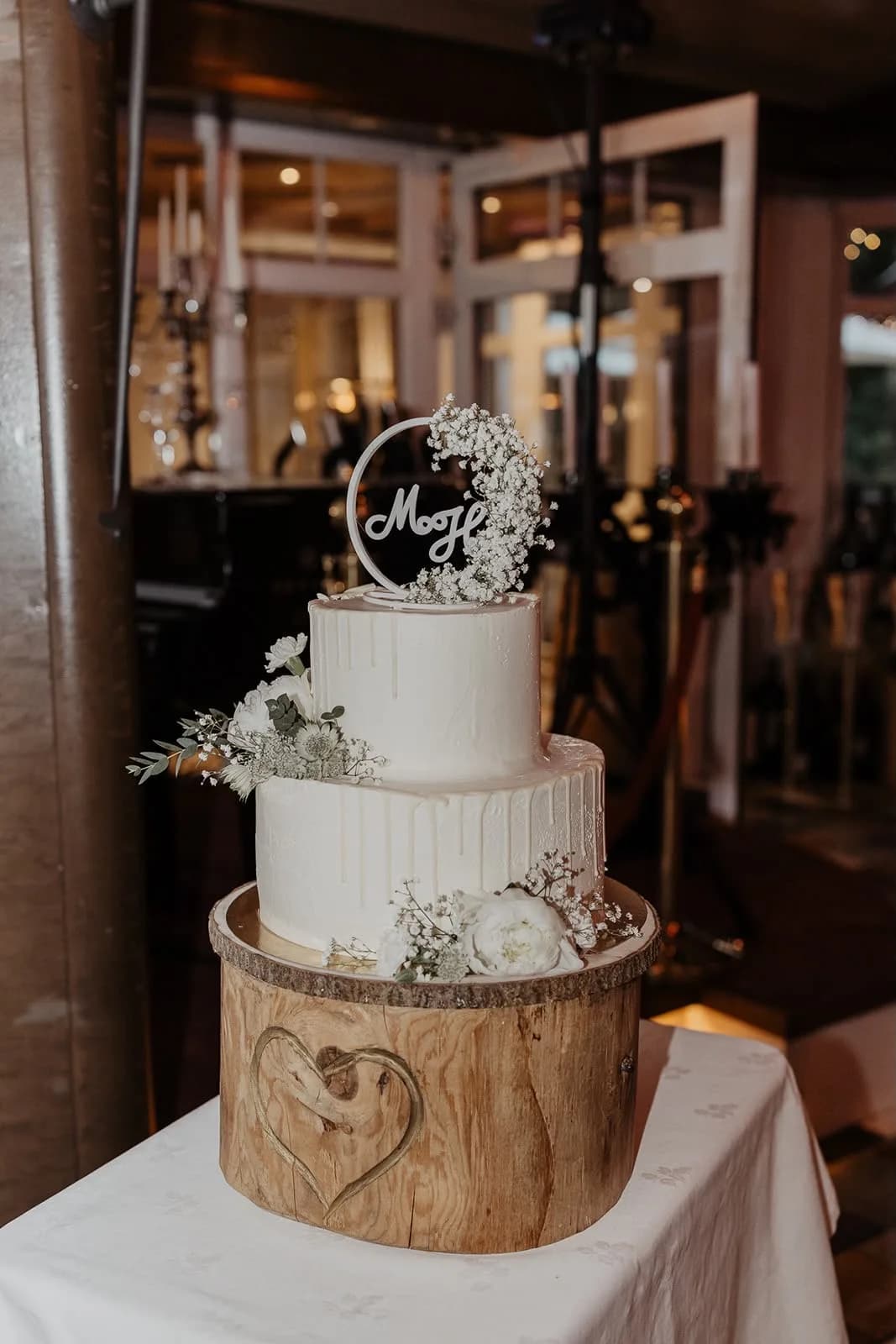 Zweistöckige weiße Hochzeitstorte mit Schleierkraut auf einem Baumstamm, aufgebaut in der Hochzeitslocation