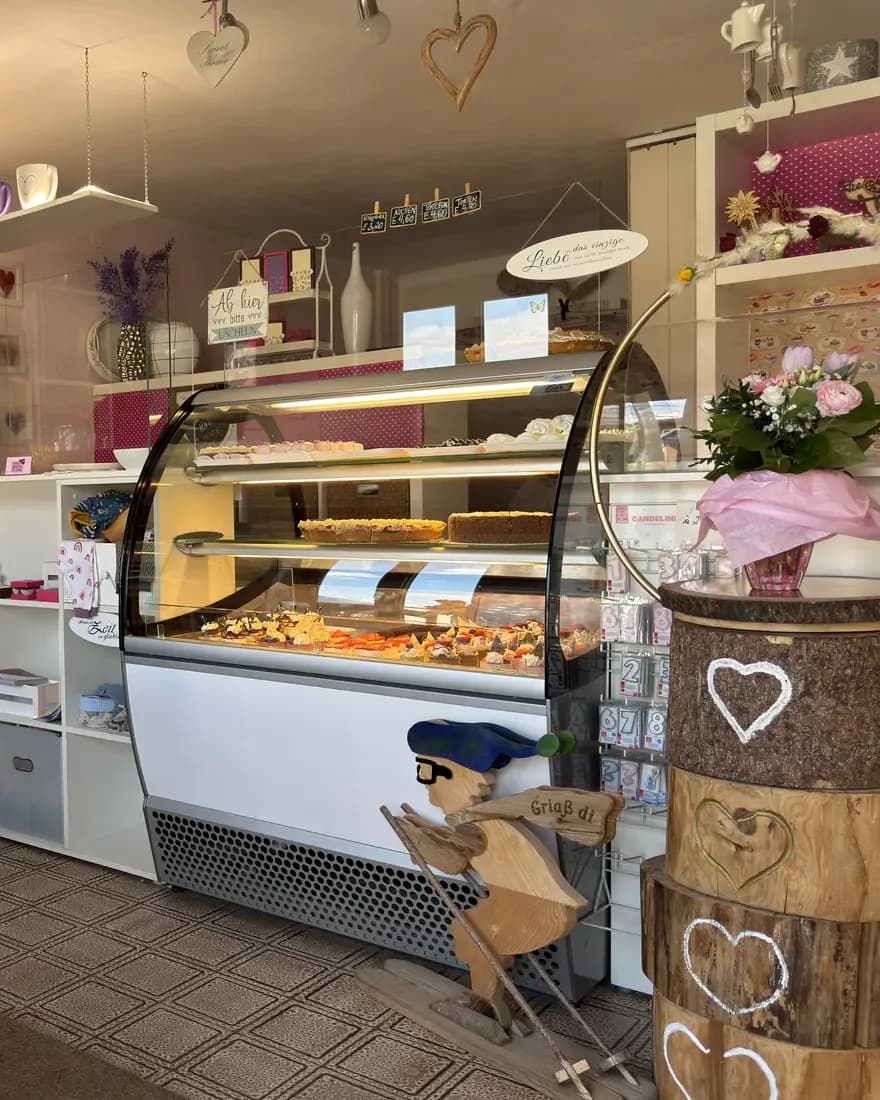Der Verkaufsraum von Silvias Backstube: die Tortenvitrine mit Törtchen und Kuchen, daneben ein Blumenstrauß auf einem Holzfass