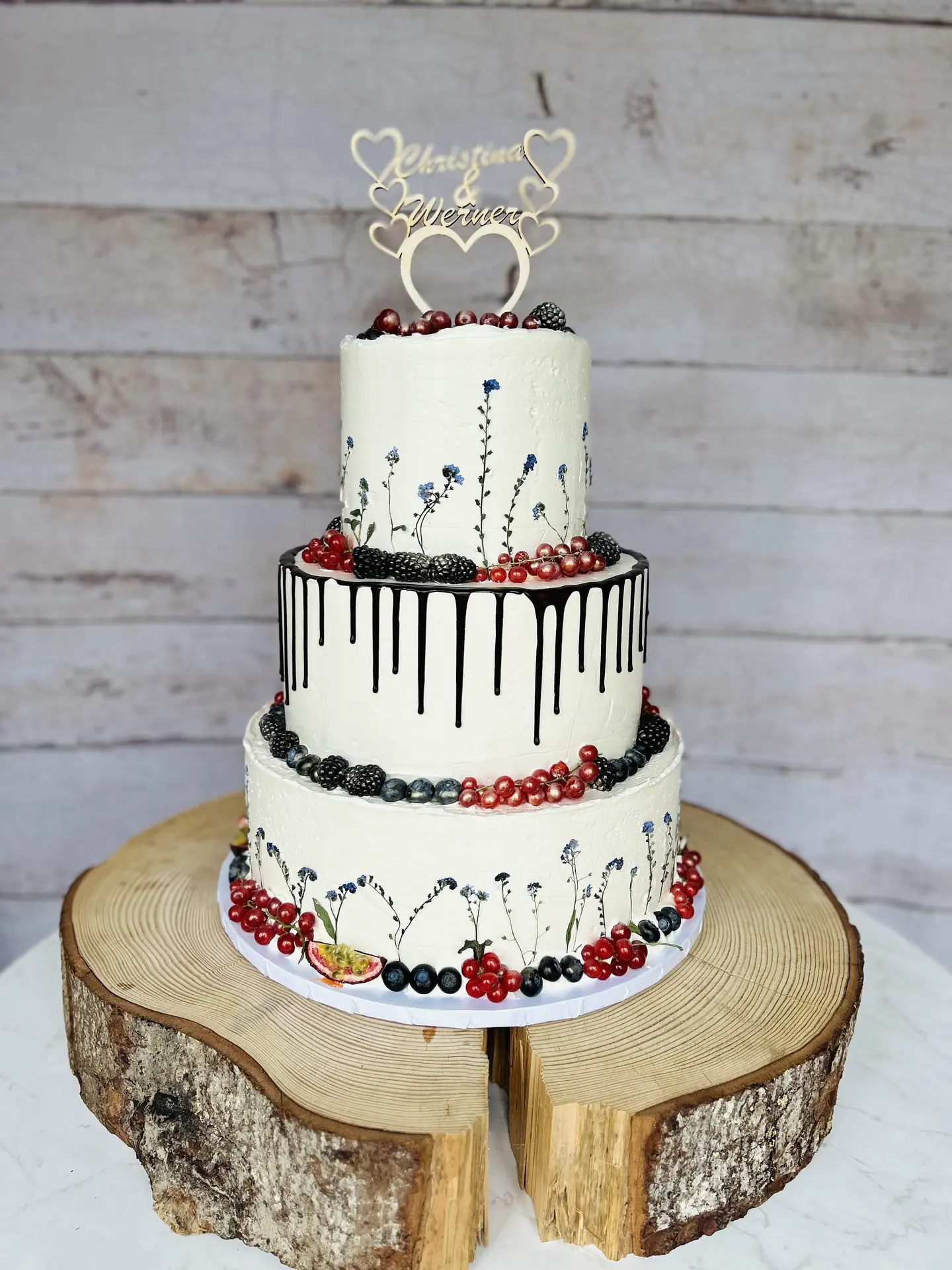 Dreistöckige Hochzeitstorte mit handgemalten Wiesenblumen, Schokoladendrip und frischen Beeren