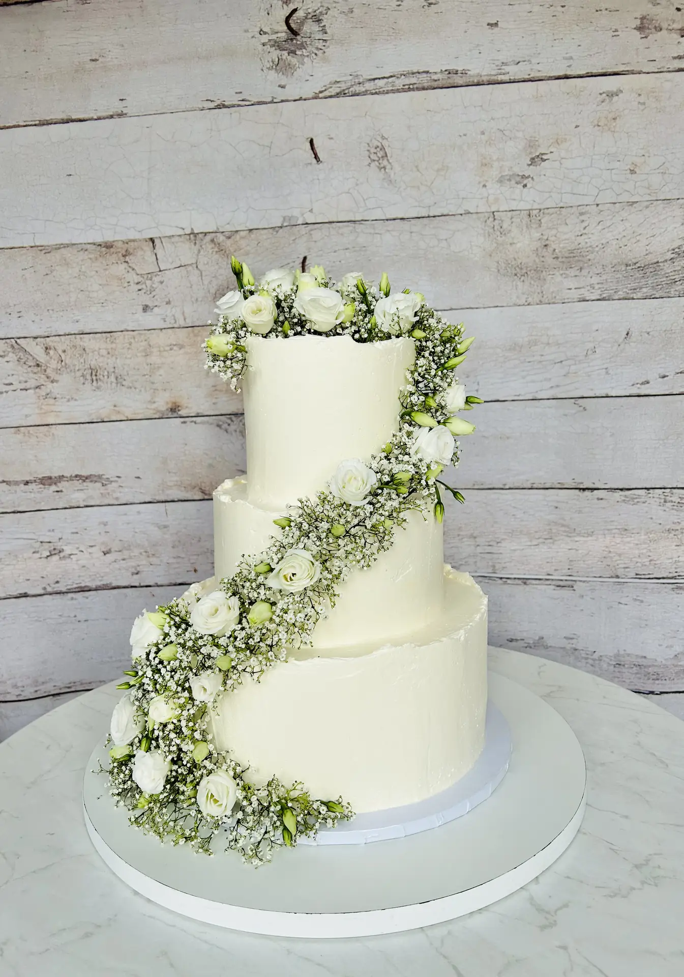 Dreistöckige weiße Hochzeitstorte mit kaskadierenden weißen Rosen und Schleierkraut