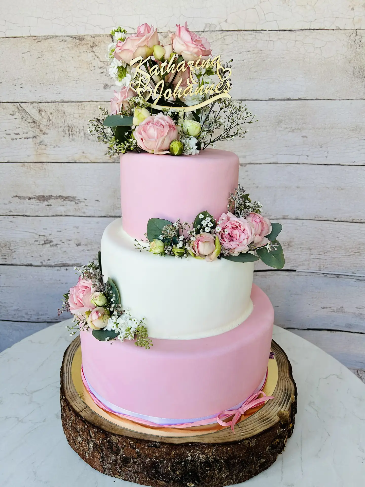 Dreistöckige rosa-weiße Hochzeitstorte mit Pfingstrosen und goldenem Namens-Topper