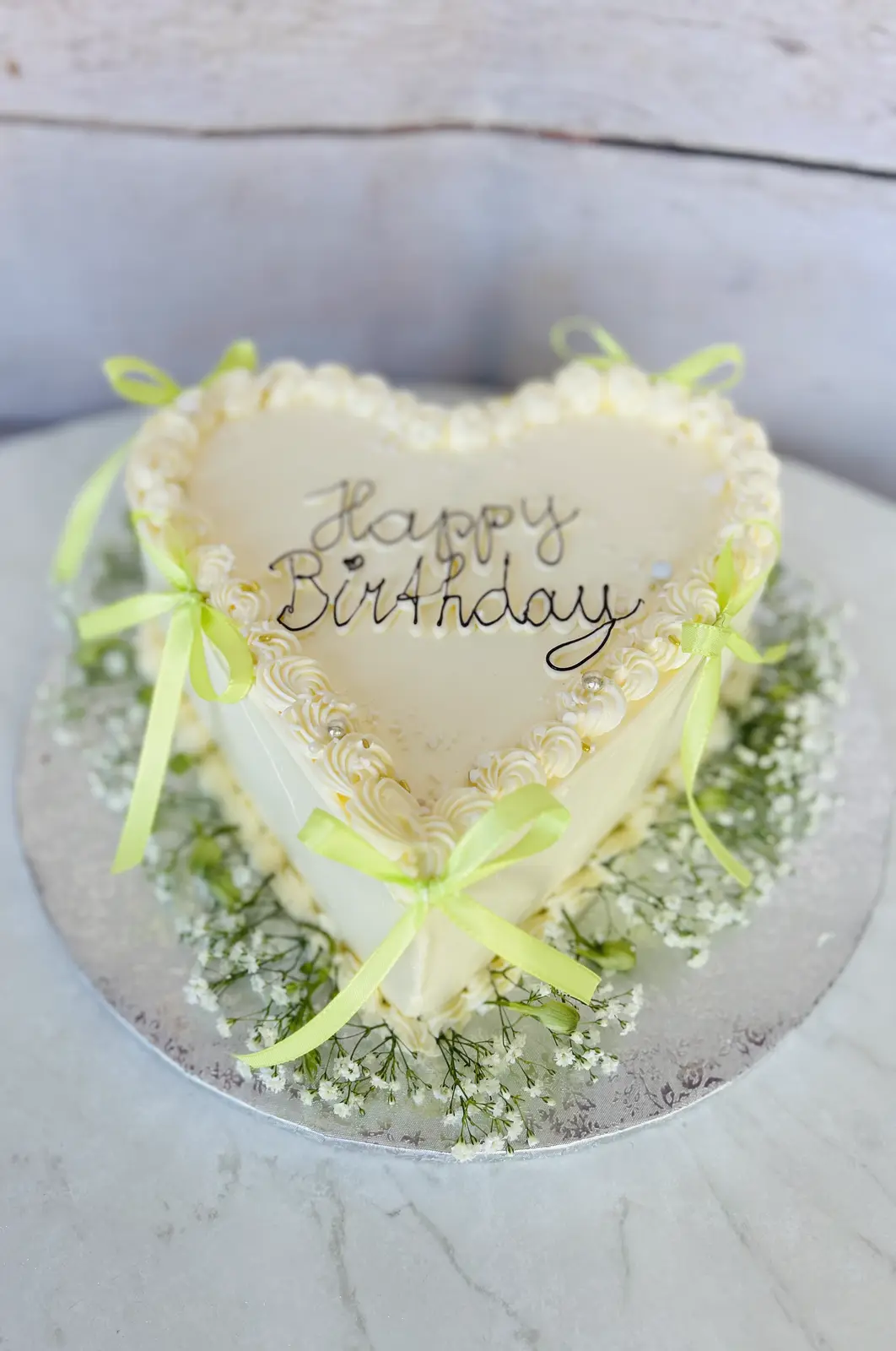 Herzförmige Happy-Birthday-Torte mit grünen Schleifen und Schleierkraut