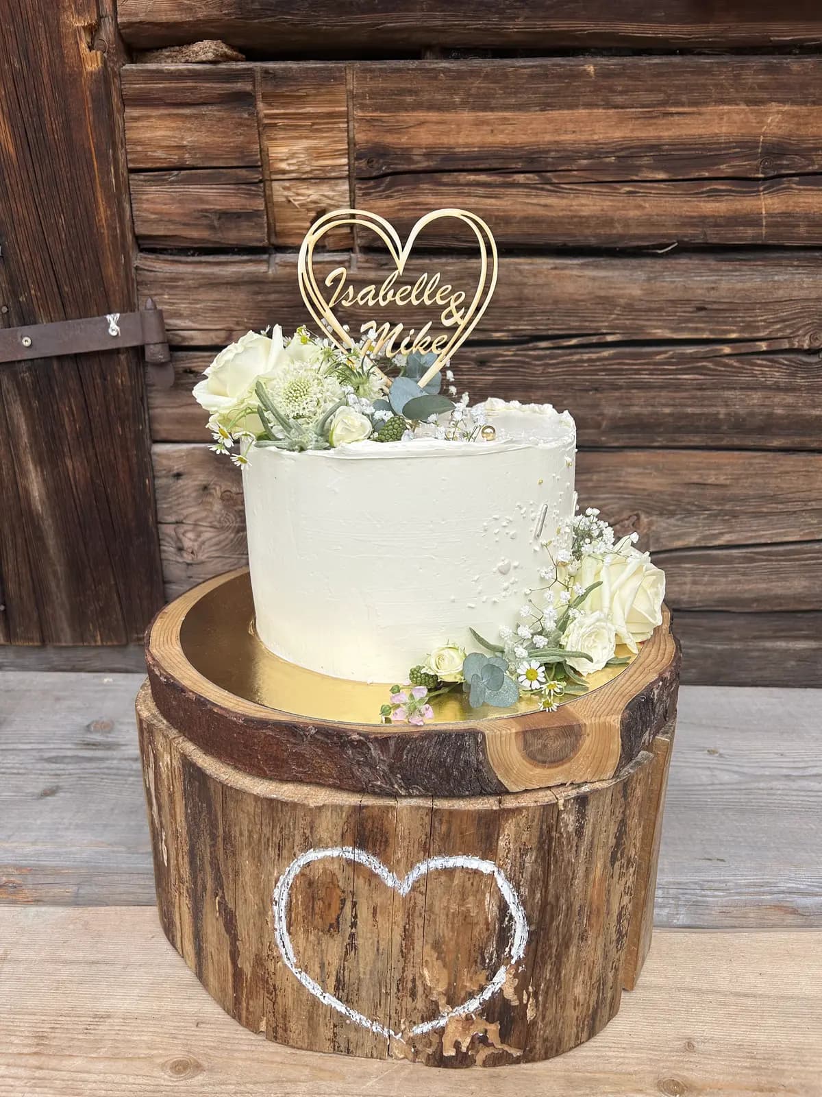 Rustikale Hochzeitstorte auf Baumstamm mit weißen Rosen und Herz-Topper