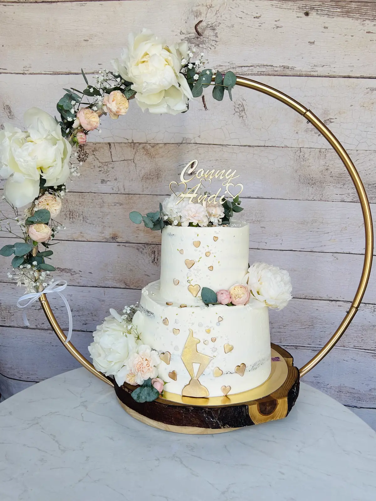 Zweistöckige Hochzeitstorte mit goldenen Herzen im Blumenreif