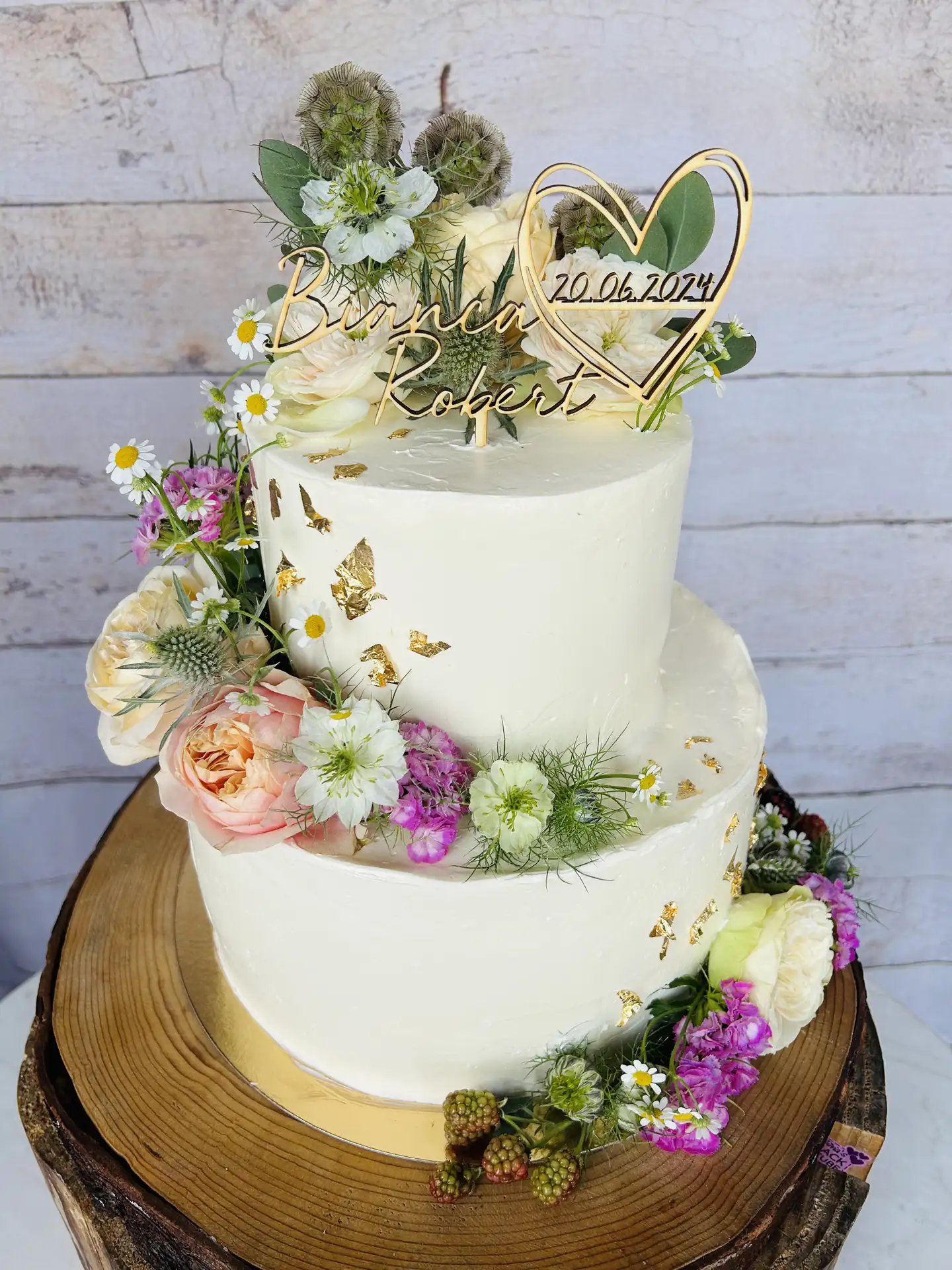 Zweistöckige weiße Hochzeitstorte mit Wiesenblumen und Blattgold