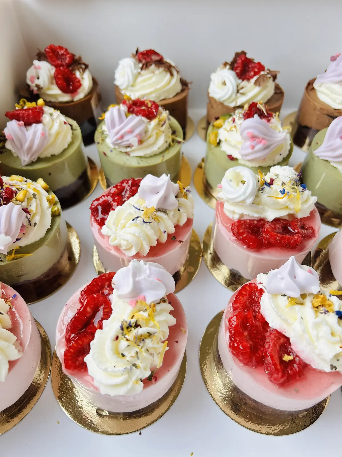 Auswahl an Himbeer-, Pistazie- und Schokoladen-Törtchen auf Goldtellern