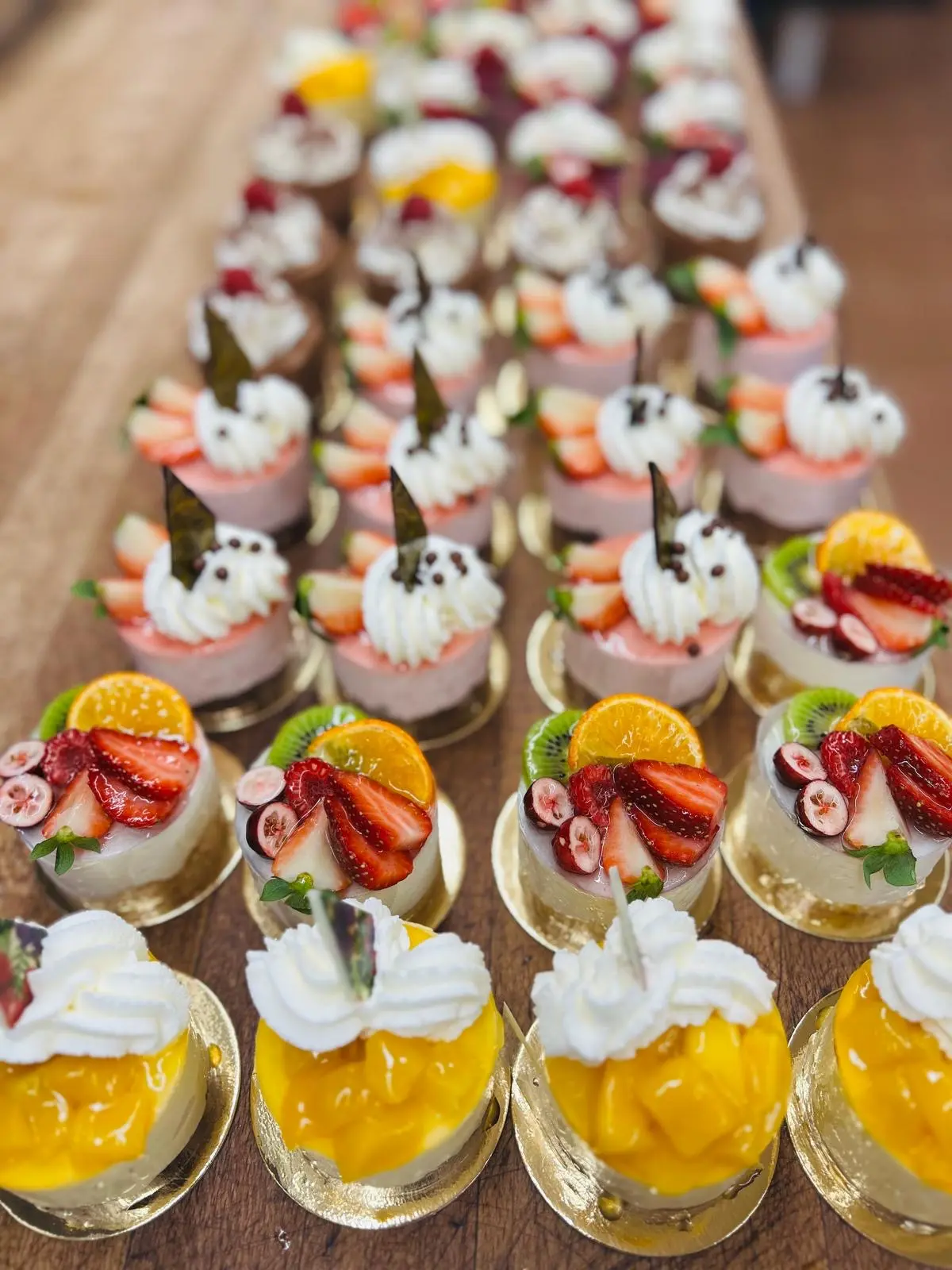 Reihen von bunten Mini-Törtchen mit Erdbeeren, Mango und Kiwi